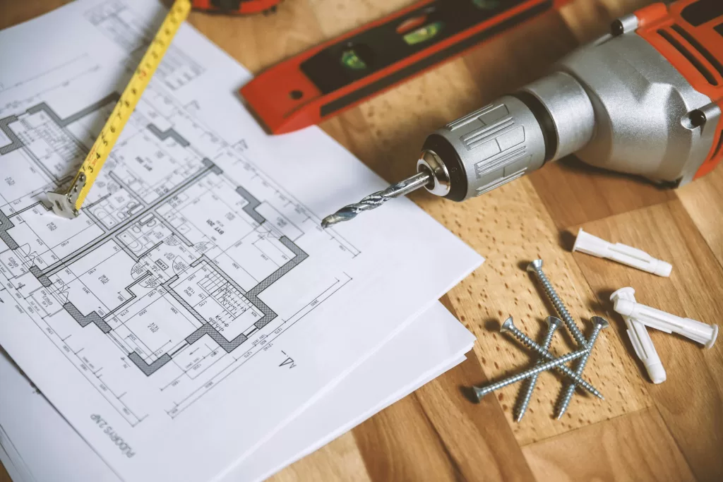 a blueprint and drill on table with nails