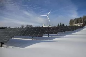 solar panels in the snow in front of a giant windmill