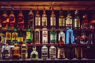 a bar in a remodeled man cave basement with liquor bottles and nice lighting and shelving