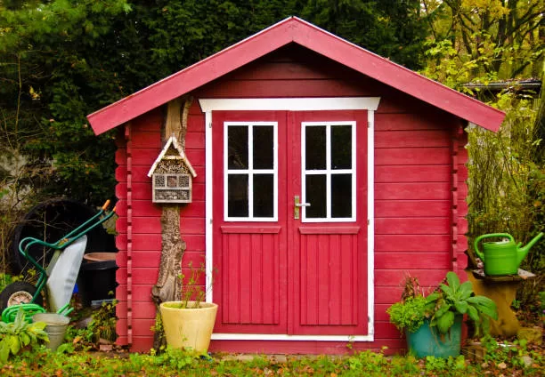 A light red small she-shed, gardenhouse, with some garden tools around it
