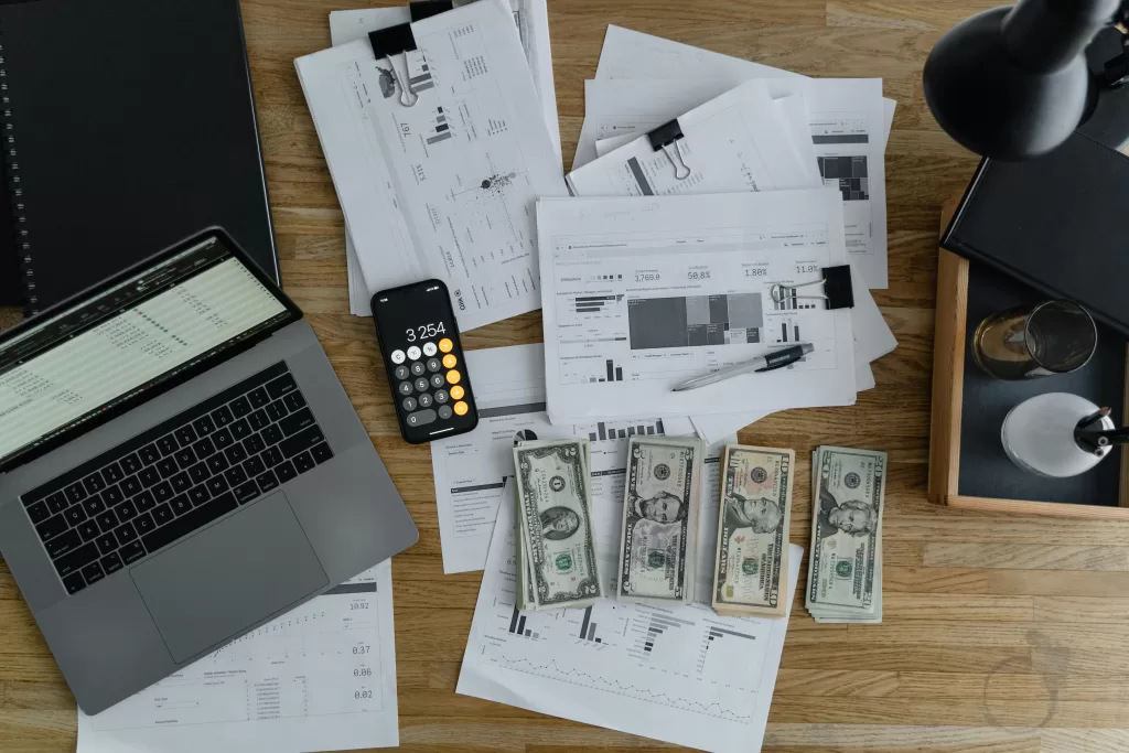 Money and a calculator with some papers near a laptop, showing a budget plan