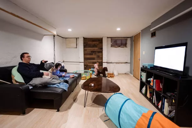 A father with two daughters (toddler age) watching tv in their basement family room of their home. They are dressed casually for relaxing at home.