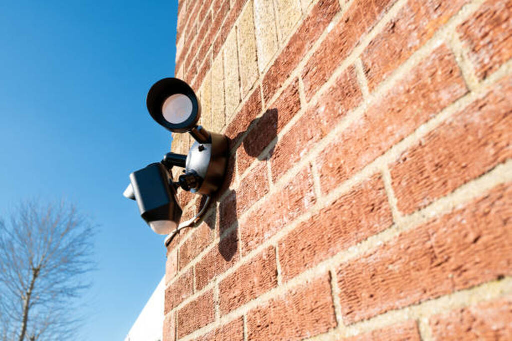 Motion activated LED floodlight with security camera mounted above Toronto backyard wall.